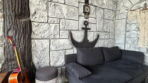 A room with a stone wall, a black sofa, a patterned ottoman, a guitar, and an anchor decoration. - Villas Rustica Fethiye (Fethiye)
