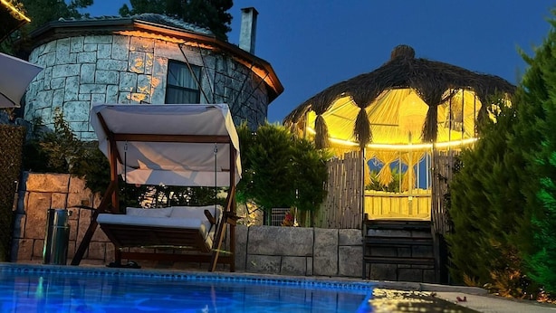 A swimming pool with a lounge chair and umbrella, a stone building with a thatched-roof structure, and a well-lit pathway leading to the building. - Villas Rustica Fethiye (Fethiye)