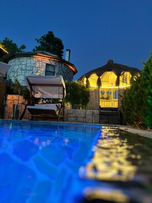 A swimming pool with a lounge chair and umbrella, a stone building with a thatched-roof structure, and a well-lit pathway leading to the building. - Villas Rustica Fethiye (Fethiye)