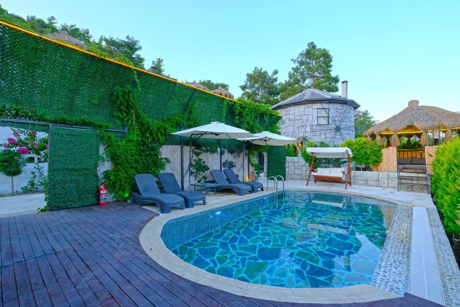 A swimming pool with lounge chairs, a stone building, and a thatched-roof structure.