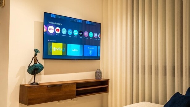 Et moderne hotelværelse med et fladskærms-tv på væggen, der viser forskellige streamingtjenester.