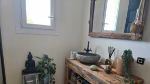 Ein Badezimmer mit einem rustikalen Holzwaschtisch, einem SteinklopfZuber, einer Buddha-Statue und einem Spiegel.