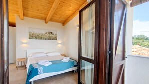 Een slaapkamer met een houten plafond, een bed met een blauwe sprei, een glazen deur en een schilderij aan de muur.