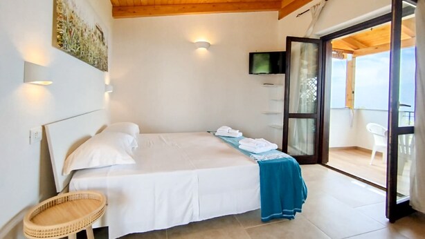 Een slaapkamer met een bed, een televisie, een balkon met een stoel en een houten plafond.