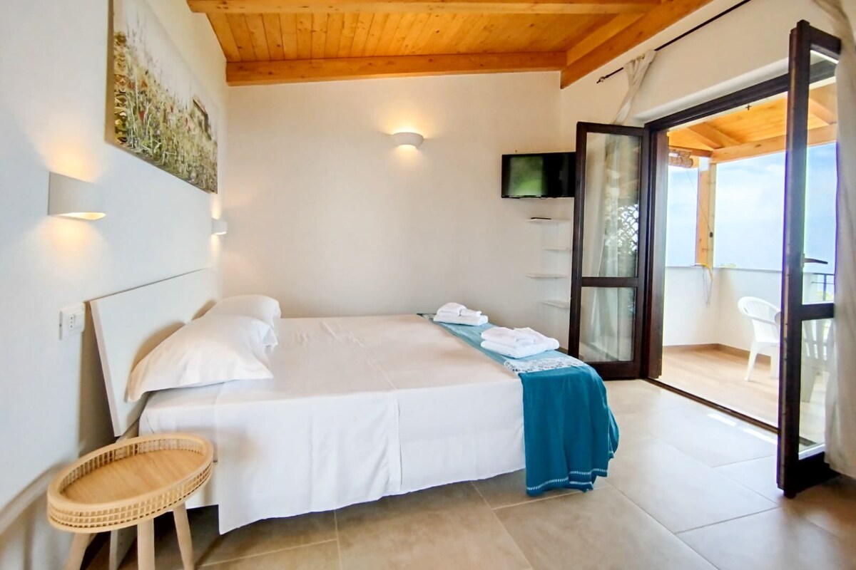 A bedroom with a bed, a TV, a balcony with a chair, and a wooden ceiling.