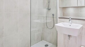 Een moderne badkamer met een douchecabine van glas, een wit wastafelmeubel en een spiegel erboven.