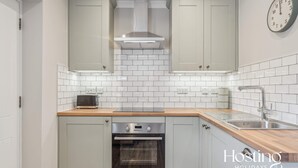 Une cuisine moderne avec des meubles de couleur gris clair, un four en acier inoxydable, un plan de travail en bois et une horloge murale.