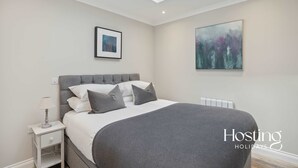 Une chambre à coucher moderne avec un grand lit, une table de chevet, une commode, un tableau encadré et une peinture au mur.