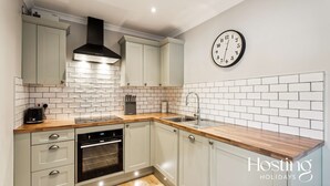 Eine moderne Küche mit hellen Schränken, einer Holz Arbeitsplatte, einem eingebauten Backofen und einer Wanduhr.