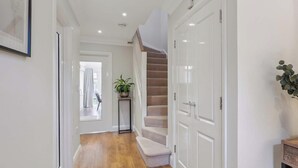 A hallway with wooden flooring, white walls, a staircase, and a potted plant. - Lavender House - Luxury 4-Bed Home with Parking - New for Spring 2026! (Maidenhead)