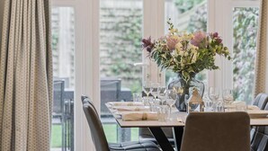 A dining area with a table set for four, a vase of flowers, and a view of greenery outside. - Lavender House - Luxury 4-Bed Home with Parking - New for Spring 2026! (Maidenhead)