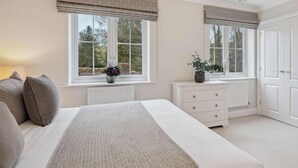 A bedroom with a bed, bedside tables, a dresser, and windows with curtains. - Lavender House - Luxury 4-Bed Home with Parking - New for Spring 2026! (Maidenhead)