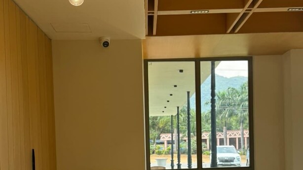 A reception area with a marble counter, a large window with a view of a parking area and greenery, and a ceiling with a light fixture.
