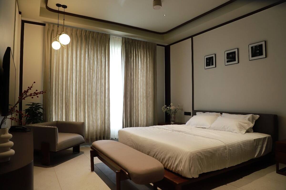 A modern bedroom with a large bed, a sofa, a bench, and a ceiling light.