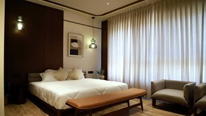 A modern bedroom with a large bed, a bench, a sofa, and a large window with curtains.