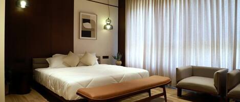 Una camera da letto moderna con un letto grande, una panca, un divano e un'ampia finestra con tende.