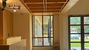 A reception area with a wooden reception desk, a large glass door leading outside, and a ceiling with exposed beams.