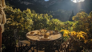 A round table with plates and bowls, surrounded by chairs, set against a mountainous backdrop with sunlight. - Can Sabuba (Deia)