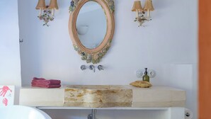 A bathroom with a large mirror, two wall-mounted lamps, a sink with a towel, and a soap dispenser. - Can Sabuba (Deia)