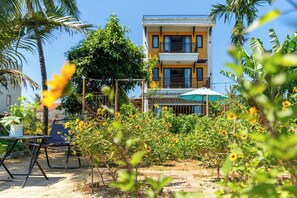 A two-story building with balconies, surrounded by greenery and a garden with yellow flowers. - Calm House 4 Hoi An (Thanh pho Hoi An)