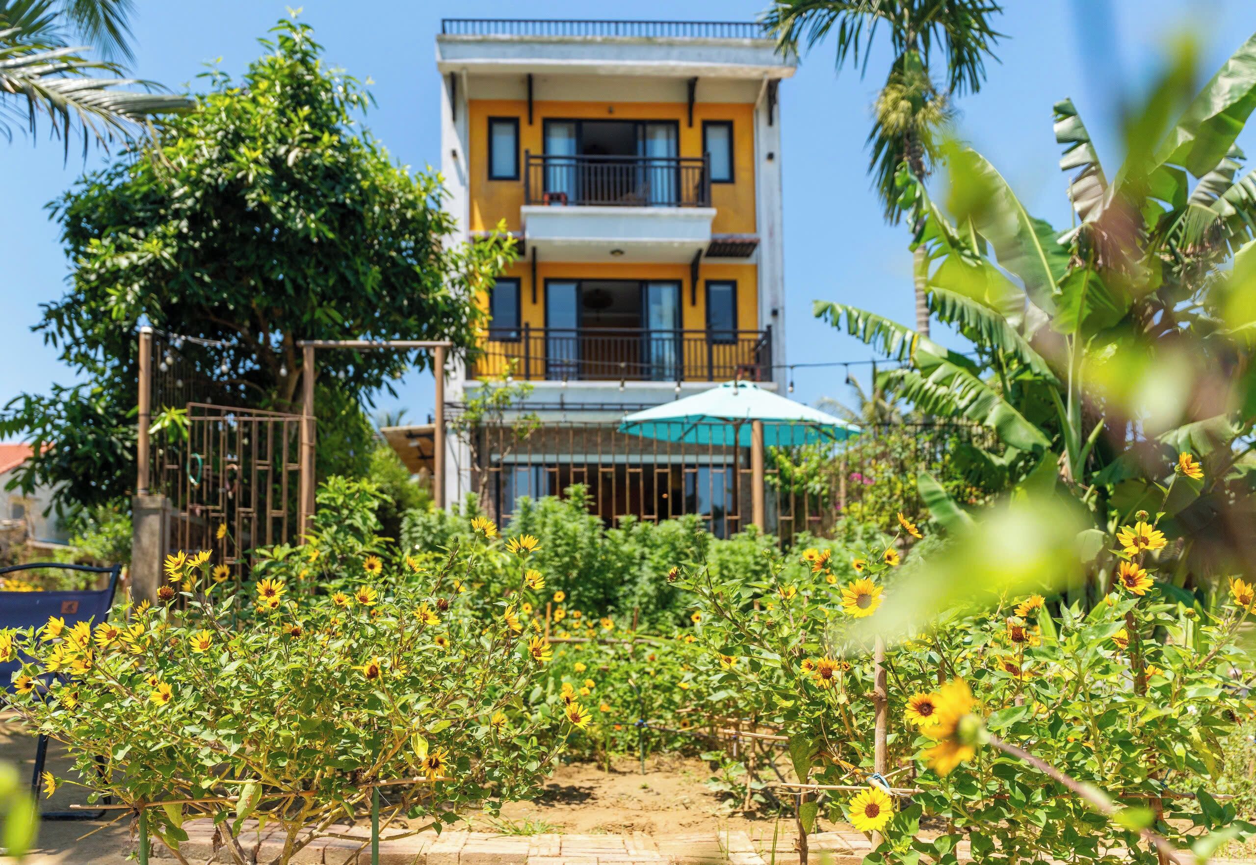 A two-story building with balconies, surrounded by a garden with sunflowers.