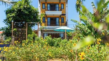 A two-story building with balconies, surrounded by a garden with sunflowers.
