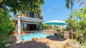 A swimming pool with a brick deck, a lounge chair, and potted plants. - Calm House 4 Hoi An (Thanh pho Hoi An)