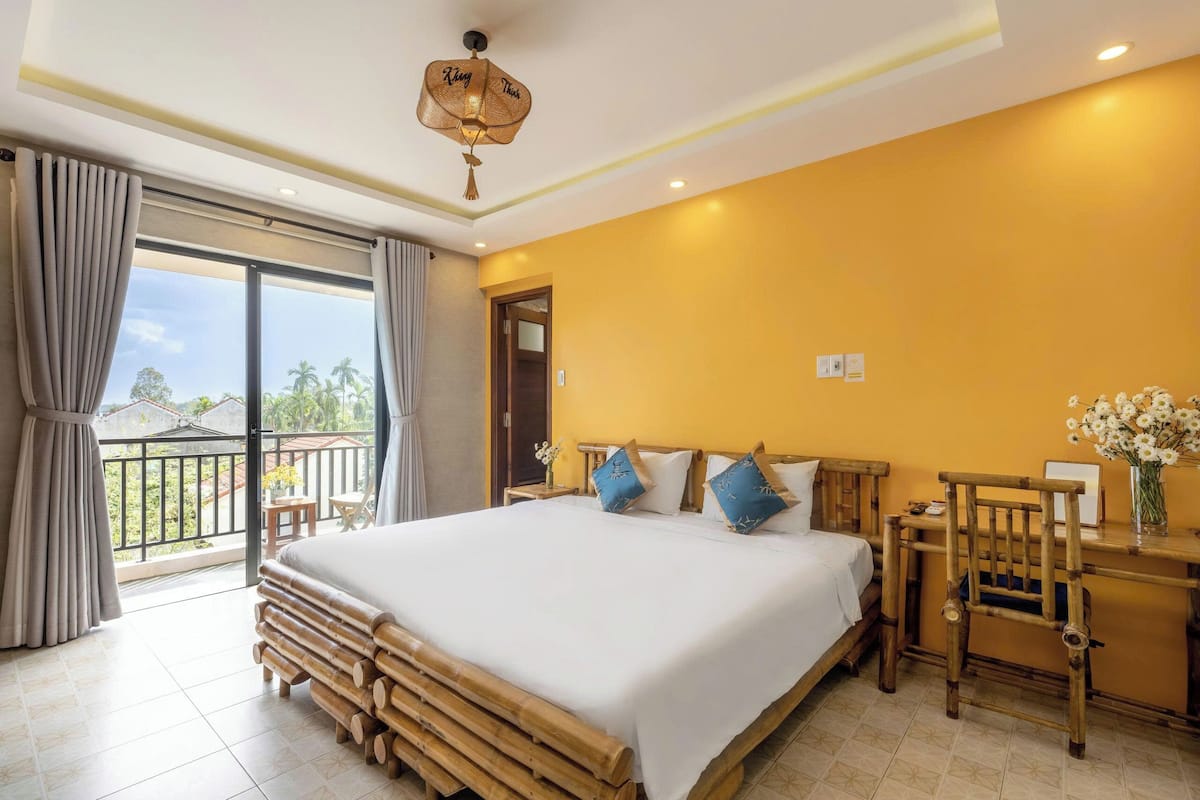 A hotel room with a large bed, a wooden desk, a chair, and a balcony with curtains.