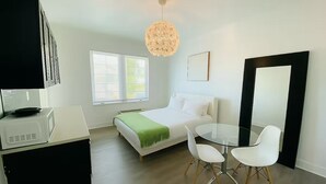 Un dormitorio moderno con cama, una mesa de vidrio con sillas, un espejo grande y una lámpara de techo.