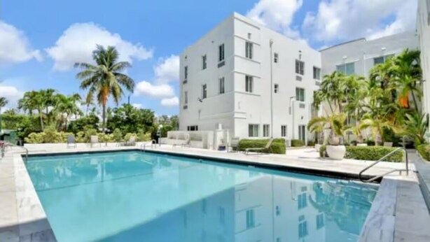 Un edificio moderno con piscina, rodeado de palmeras y vegetación.