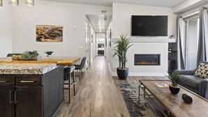 Una sala de estar moderna con chimenea, un televisor montado en la pared y una zona de comedor con una isla de cocina.