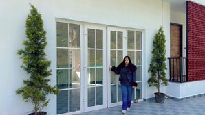 Une personne se tient devant un bâtiment doté d’une porte en verre et de deux plantes en pot.