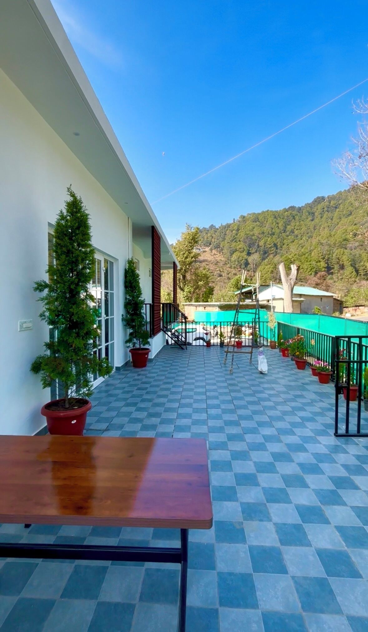 Eine Terrasse mit Schachbrettboden, Blumentöpfen und Blick auf eine Berglandschaft.