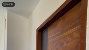 Une porte en bois avec une enseigne sur laquelle on peut lire « BASANTI » et une petite décoration florale.