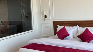 Une chambre à coucher avec un grand lit, des murs blancs, un ventilateur de plafond et une fenêtre avec des stores.
