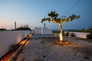A modern building with a white exterior, a gravel pathway, and a tree with illuminated lights. - Sandy Steps Beach Front Suite for 3 (Μάλια)