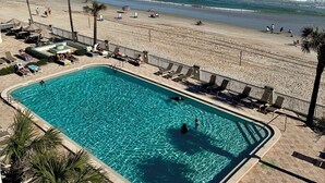 A pool area with clear blue water, adjacent to a sandy beach with palm trees and a view of the ocean. - Oceanfront 1-bedroom condo with spectacular sunrises Pool Gym Jacuzzi Sauna 🏖️ (Daytona Beach)