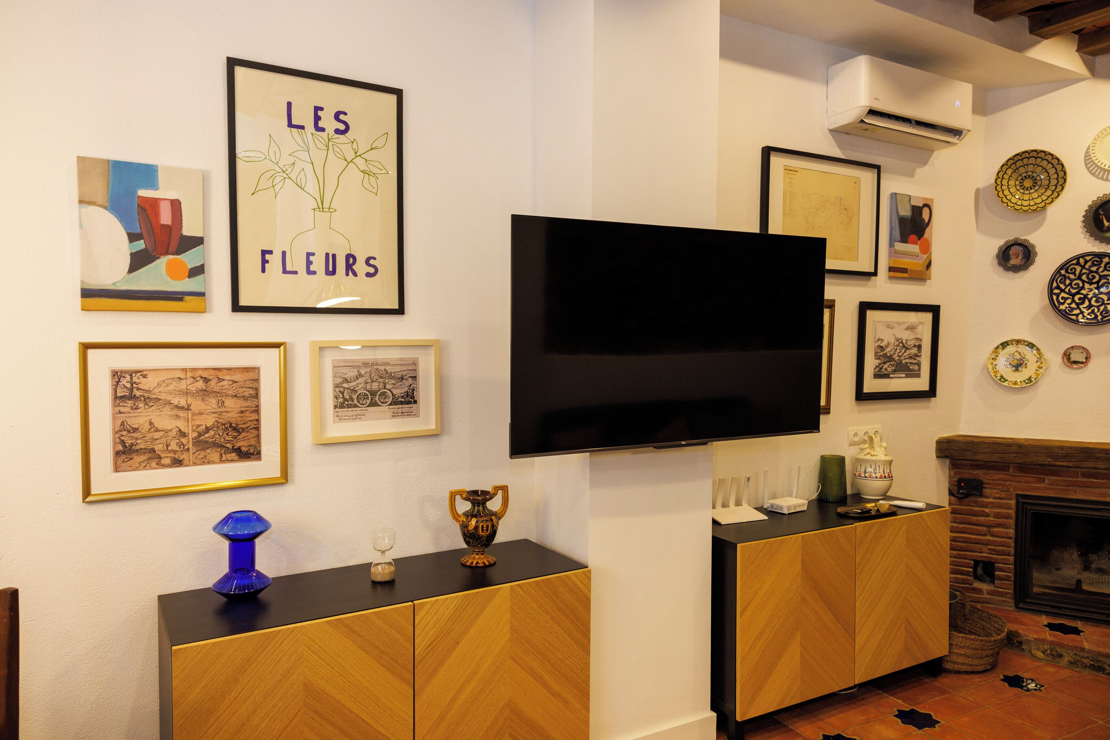 A living room with a flat-screen TV, wooden cabinets, and various framed artworks on the walls.