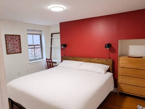 Quarto com cama, poltrona, cômoda, janela e parede com detalhe em vermelho.