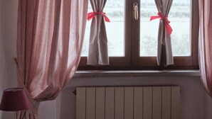 Et værelse med seng, et natbord, en lampe og et vindue med tilbagetrukne gardiner.