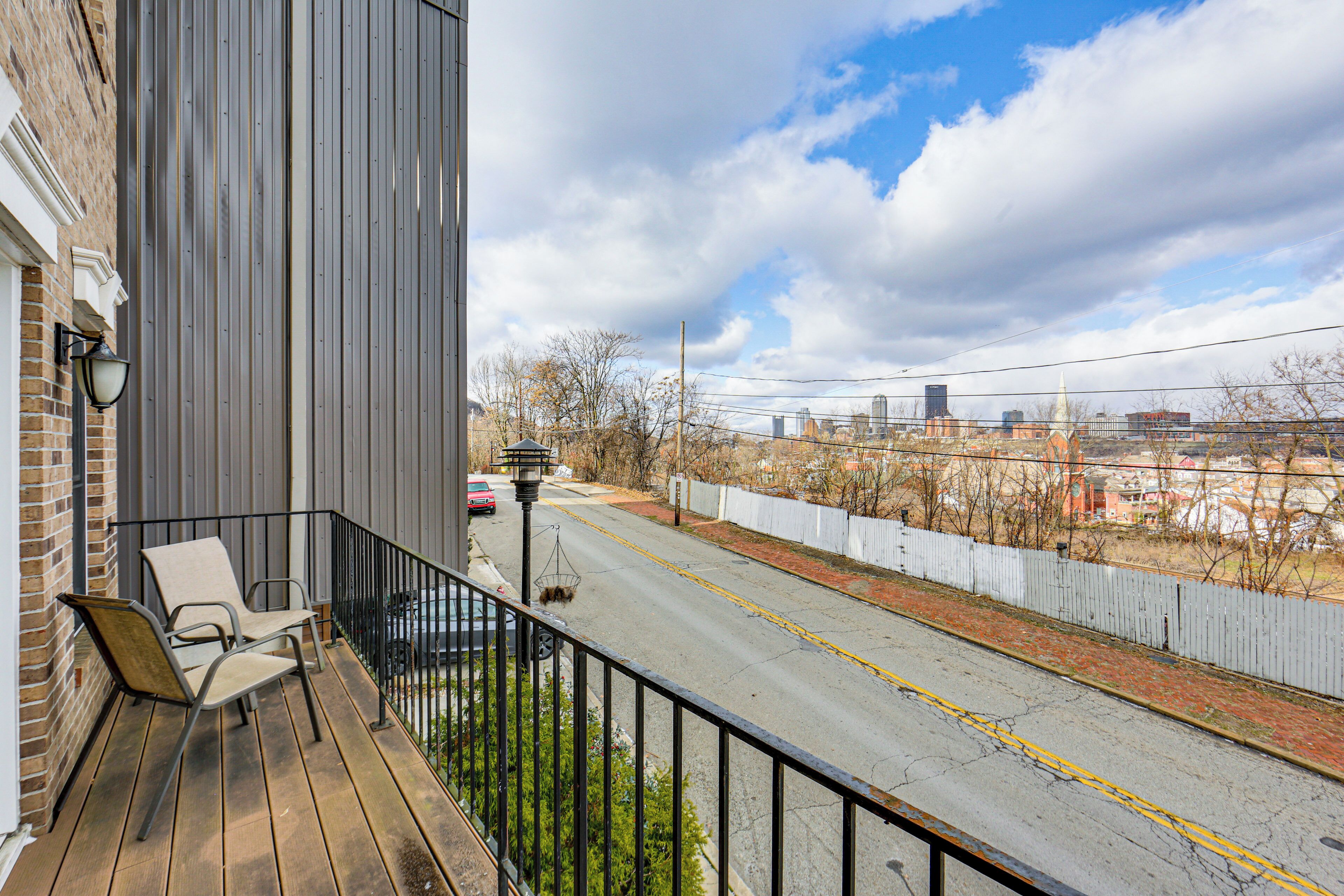 A balcony with two chairs, a street view, and a white fence.