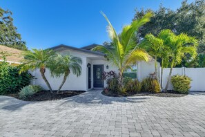 Uma casa moderna com entrada pavimentada, palmeiras e um jardim bem cuidado.