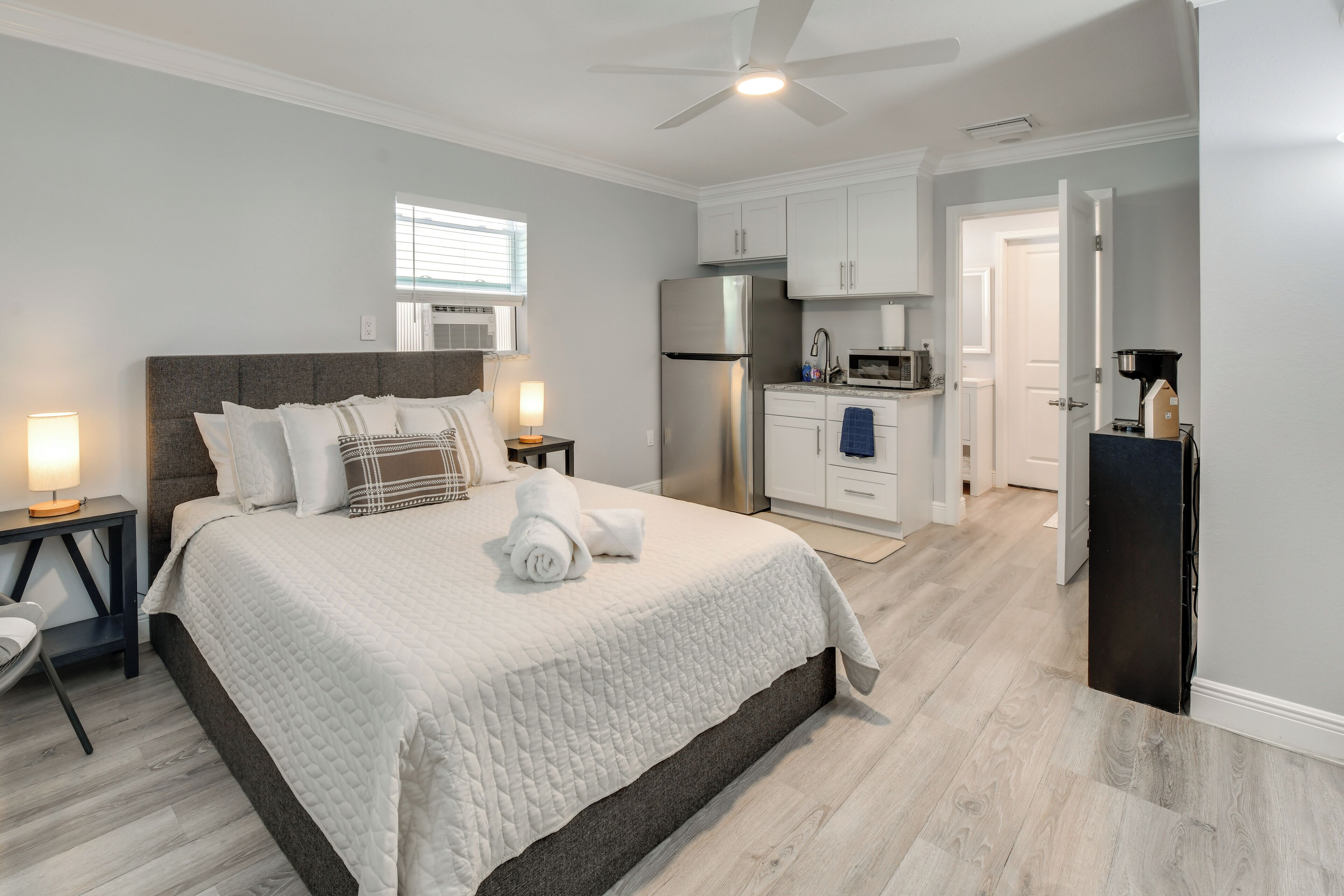 A bedroom with a bed, bedside tables, a ceiling fan, and a kitchenette.