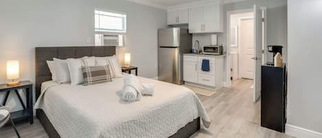 Un dormitorio con cama, mesitas de noche, ventilador de techo y kitchenette.