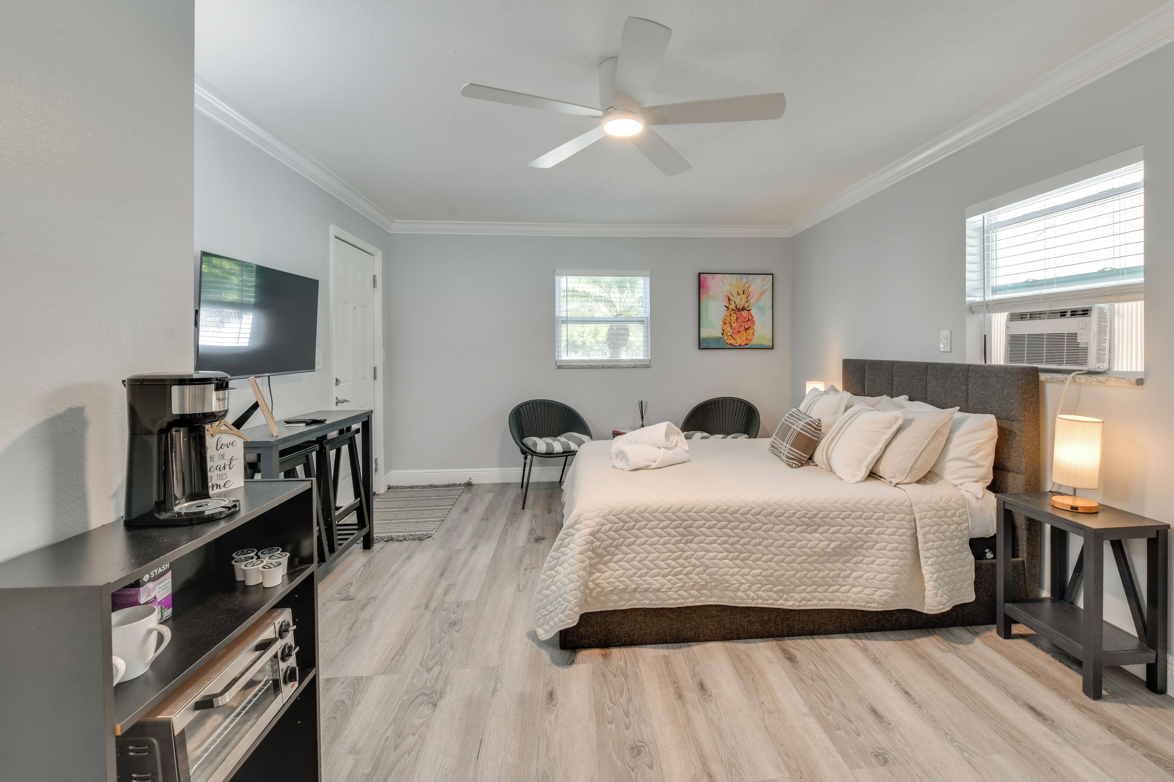 A bedroom with a bed, a ceiling fan, a TV, a coffee maker, and a small table.