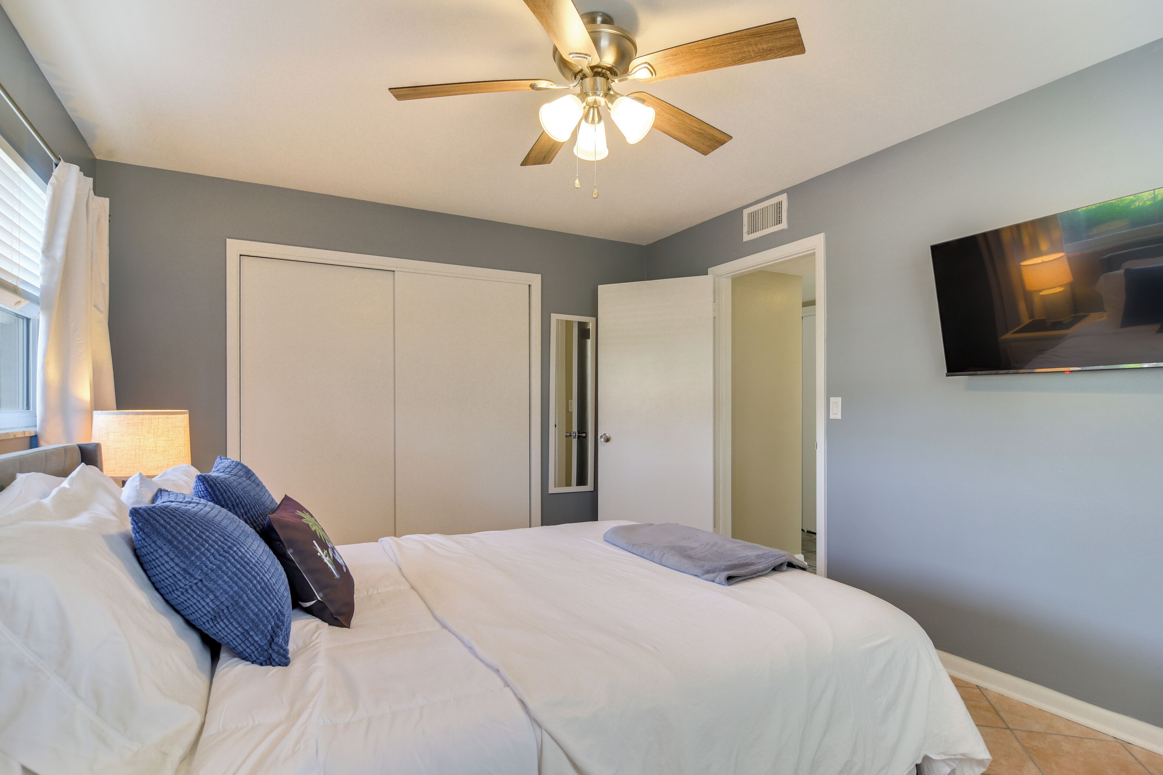 A bedroom with a bed, ceiling fan, and a TV on the wall.