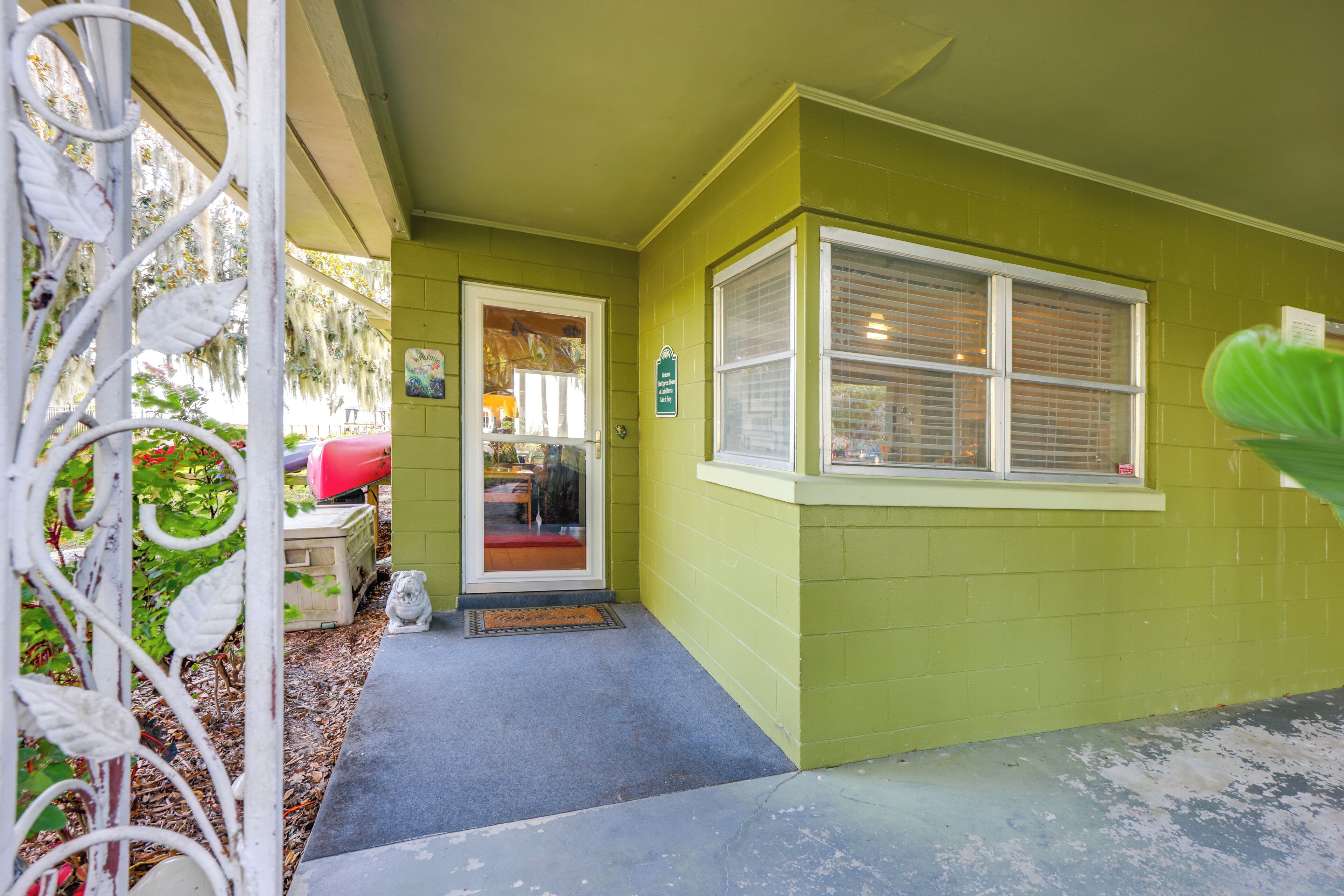 A green house with a white door, a window, and a small porch area.