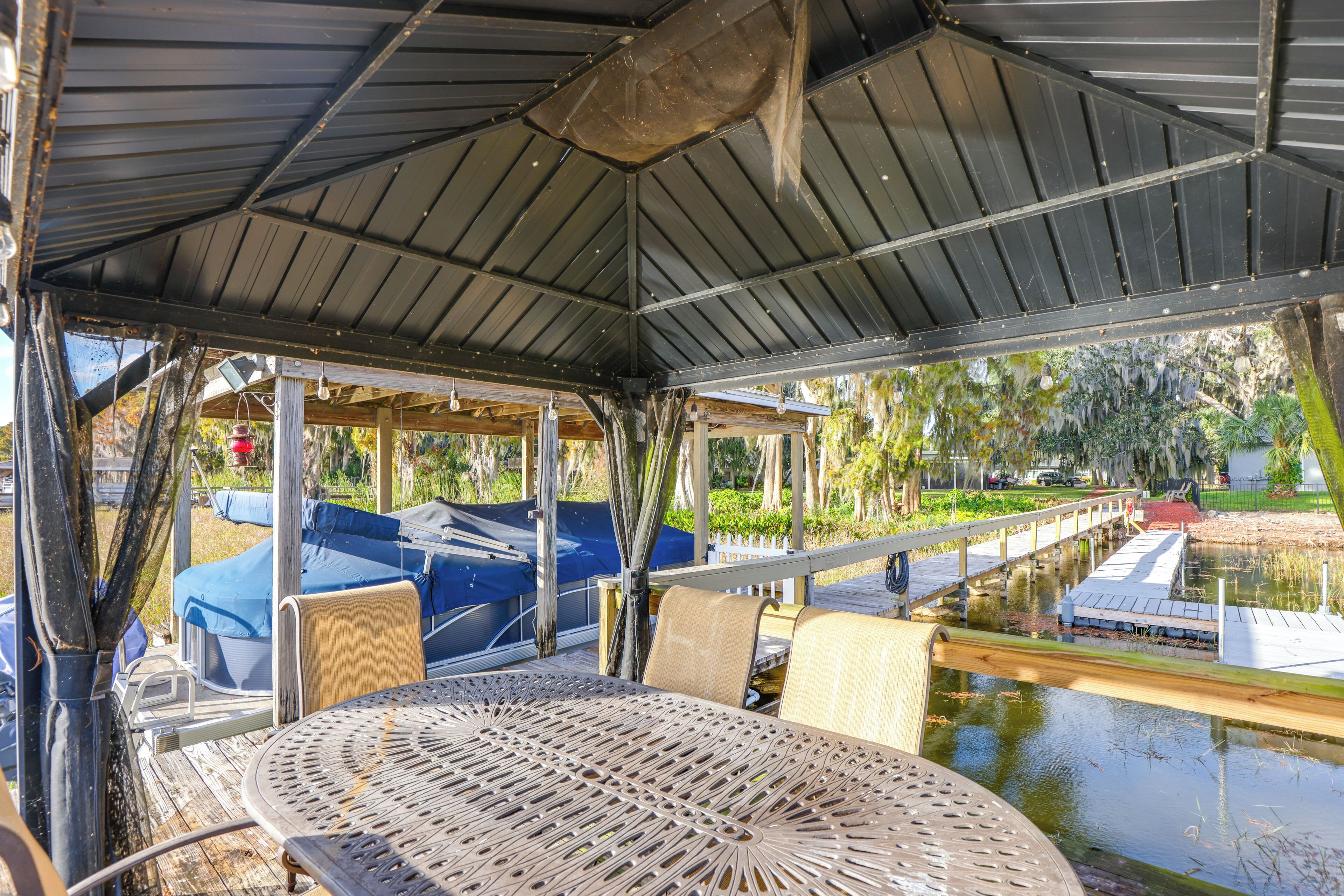 Un espace extérieur abrité, doté d’une table et de chaises, offrant une vue sur un plan d’eau et comprenant une terrasse en bois.