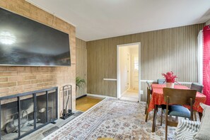 A dining area with a table set for two, a fireplace, and a large flat-screen TV mounted on a brick wall. - Convenient + Cozy! Apartment in DC Suburbs! (Silver Spring)