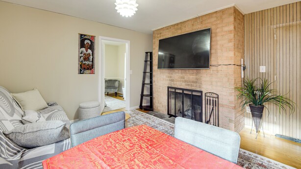 A living room with a fireplace, a flat-screen TV mounted on a brick wall, and a large red rug. - Convenient + Cozy! Apartment in DC Suburbs! (Silver Spring)